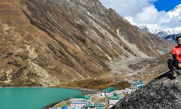 Smiling guy with victory pose - infront of Gokyo lake, Gokyo village and Mt Cho yu in the far back