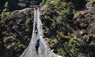 trekking over the bridge with many prayer flags