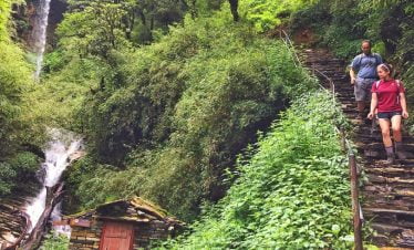 Waterfall and trekkers walking downhill in their Ghorepani Ghandruk Trekking trip in Nepal
