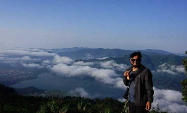 Sambit smiling at camera while the view of pokhara, lake, World peace stupa and the beautiful landscape is crystal clear in our Kathmandu Pokhara tour