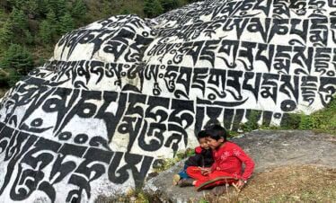 Kids playing right next to the stone encrypted with Buddhist mantra